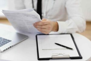 Close-up of a doctor holding medical records and reviewing a clipboard, symbolizing patient documentation and record management.