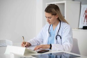 Side view of a doctor writing on a notepad with a stethoscope around their neck, emphasizing patient record maintenance.